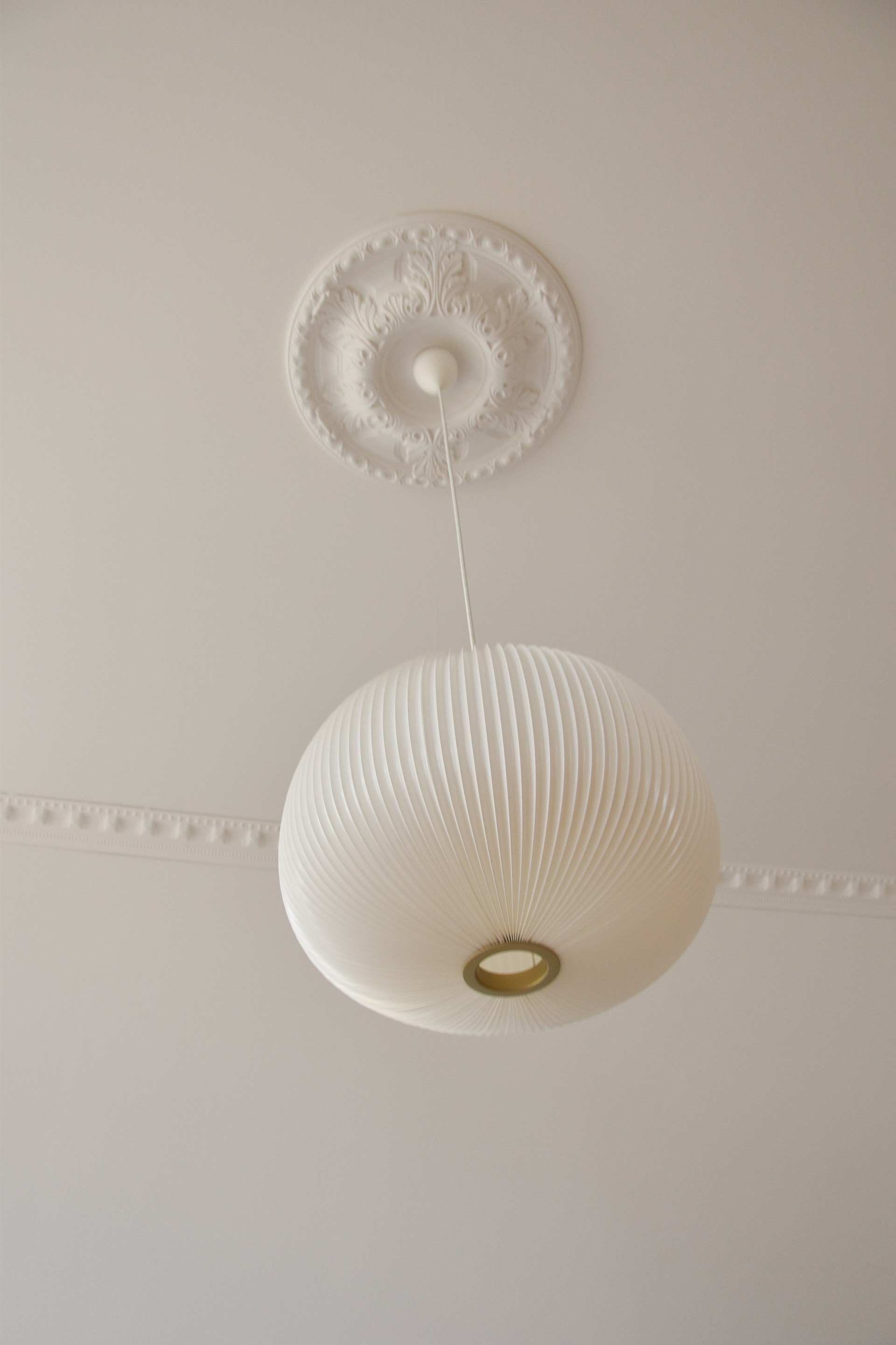 Un rosone decorato che incornicia una lampada a sospensione, abbinato a cornici discrete per una decorazione elegante del soffitto.