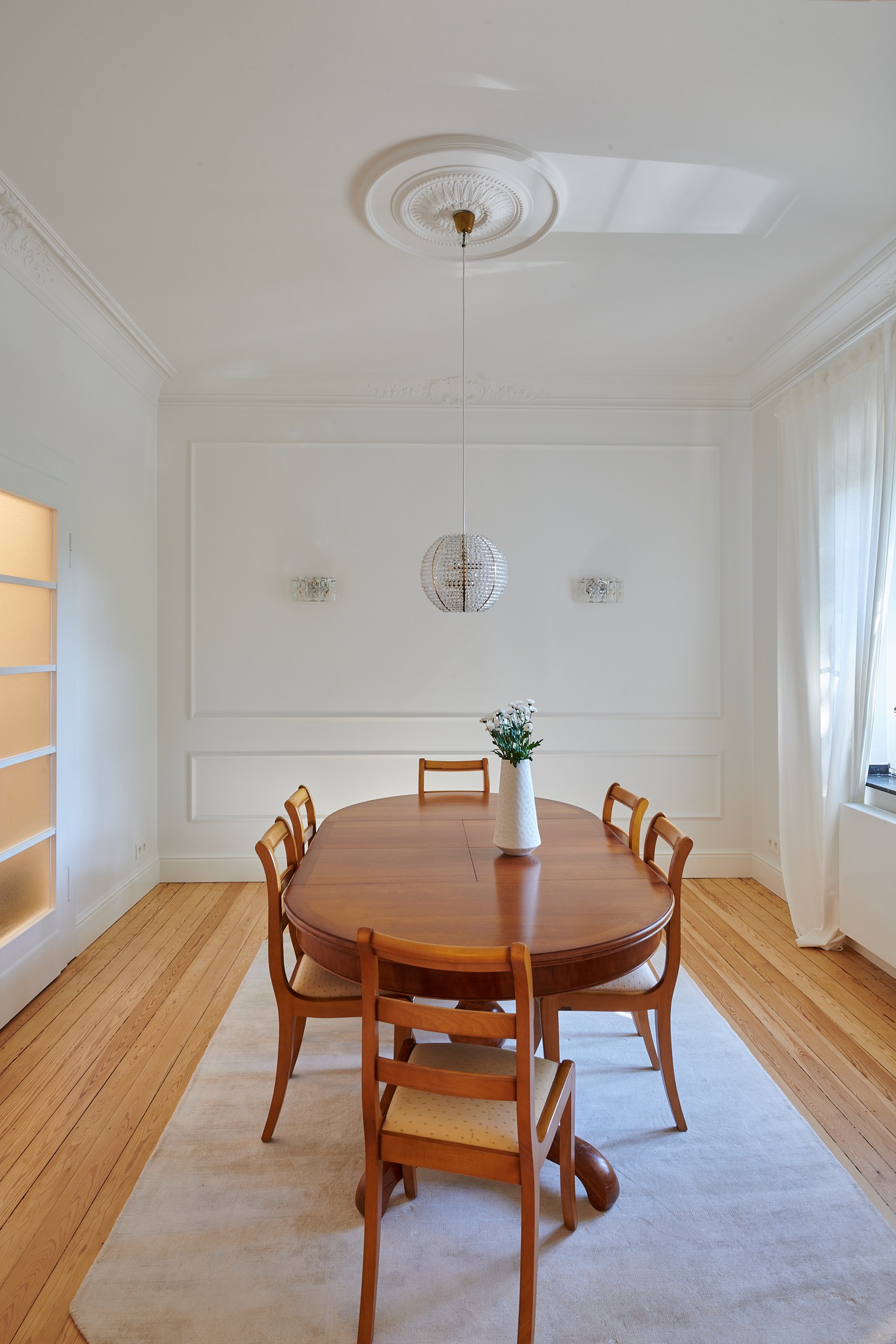 Rosone decorativo e modanature che impreziosiscono una raffinata sala da pranzo illuminata da lampadari a sospensione.