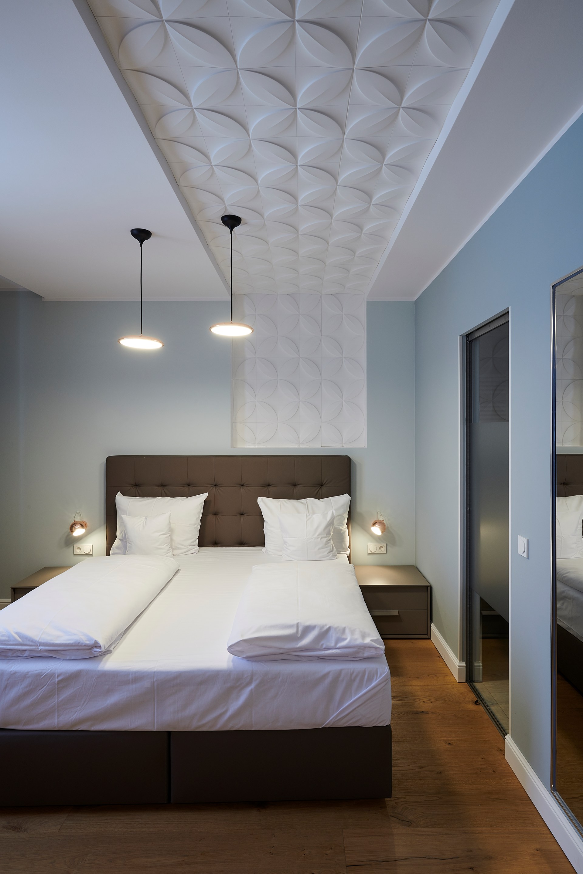 Pannelli a parete applicati al soffitto, che creano un effetto materico sopra il letto.