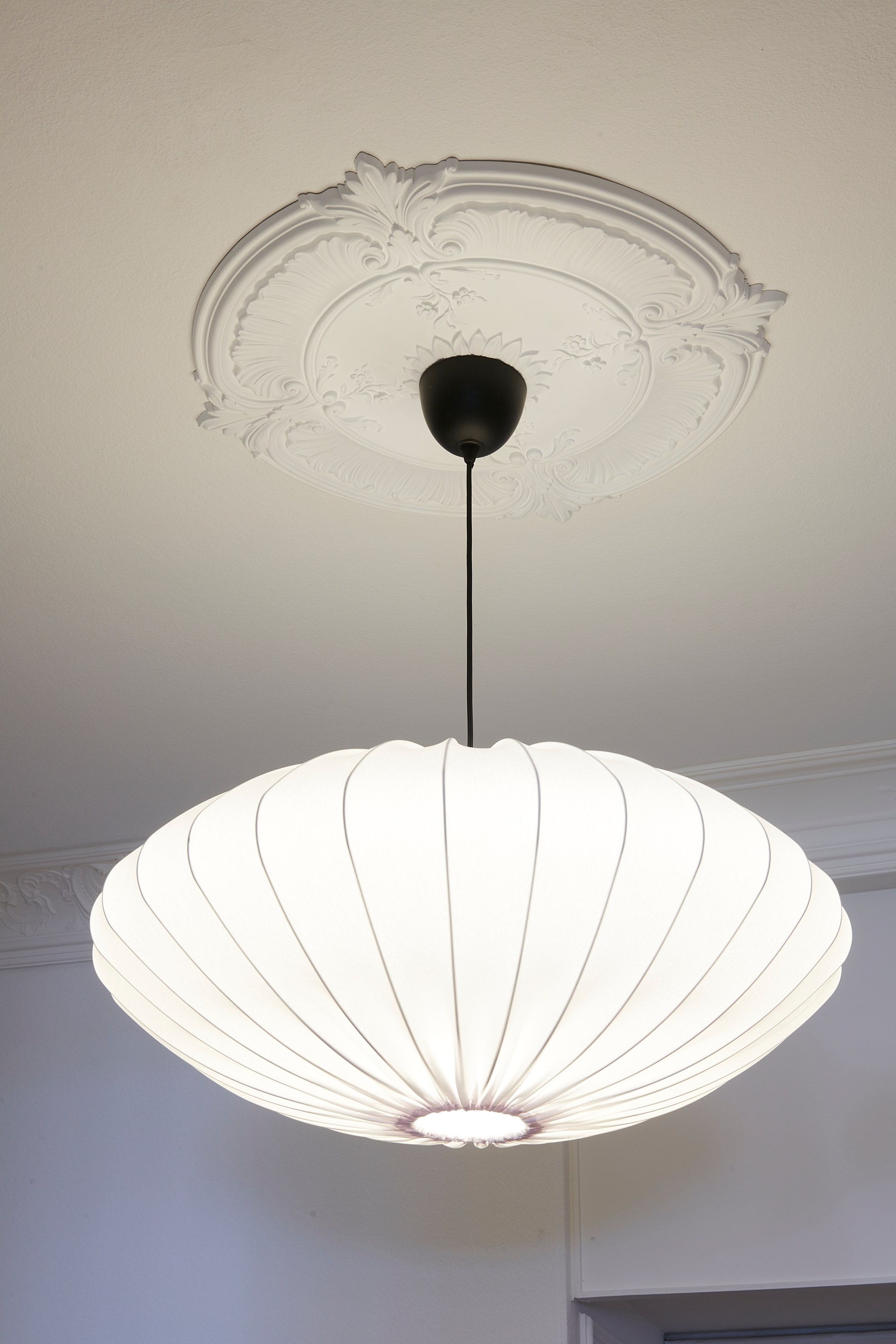 Rosone decorato con dettagli scolpiti, abbinato a una lampada a sospensione per valorizzare la decorazione classica del soffitto.